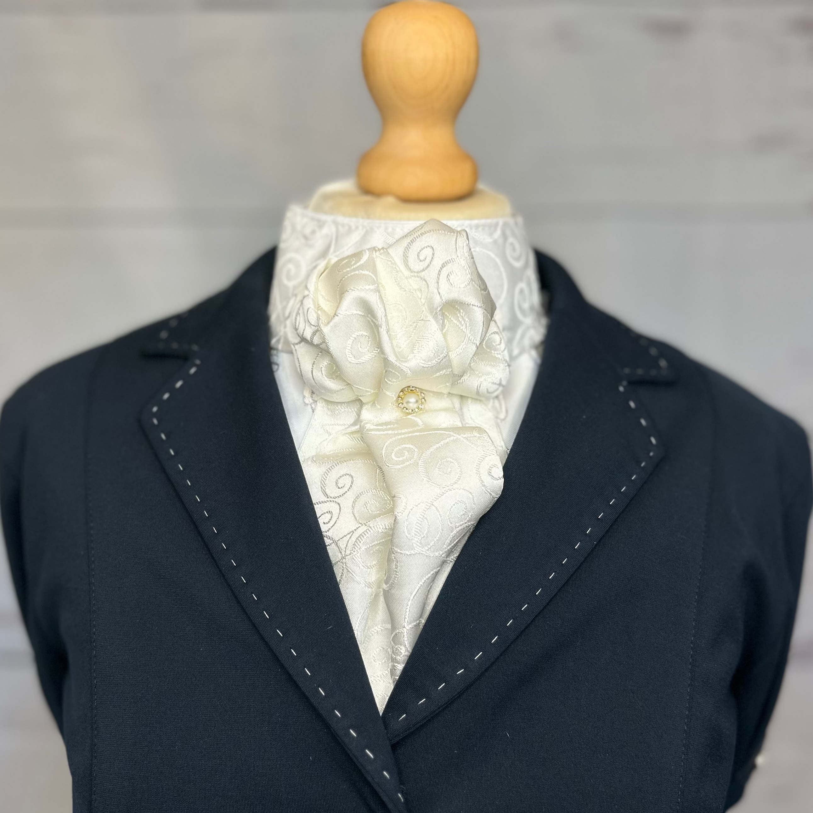 A ready tied equestrian stock tie, in ivory on a mannequin with a blue jacket. 