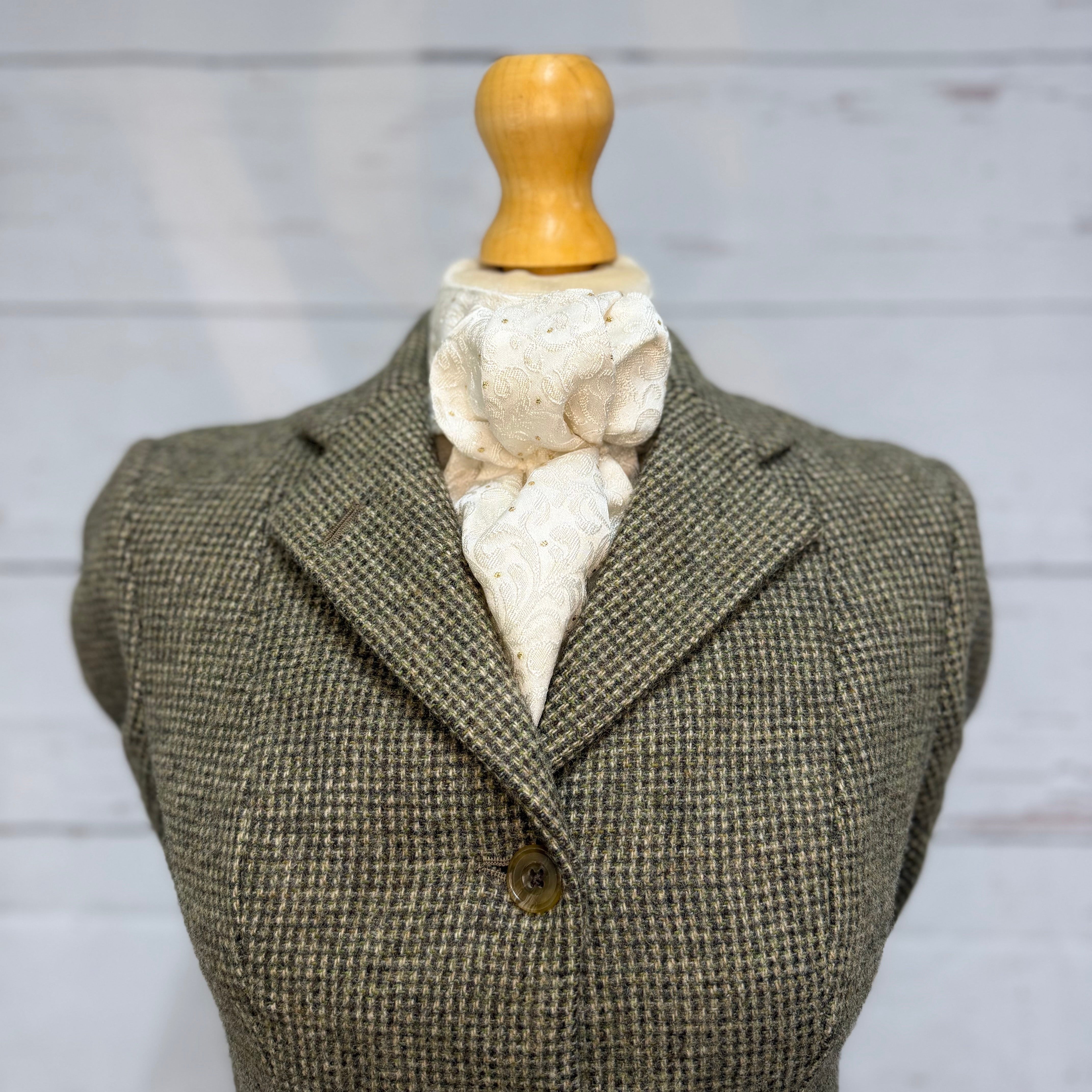 tweed jacket on a mannequin with a white and gold stock tie, soft neutral background