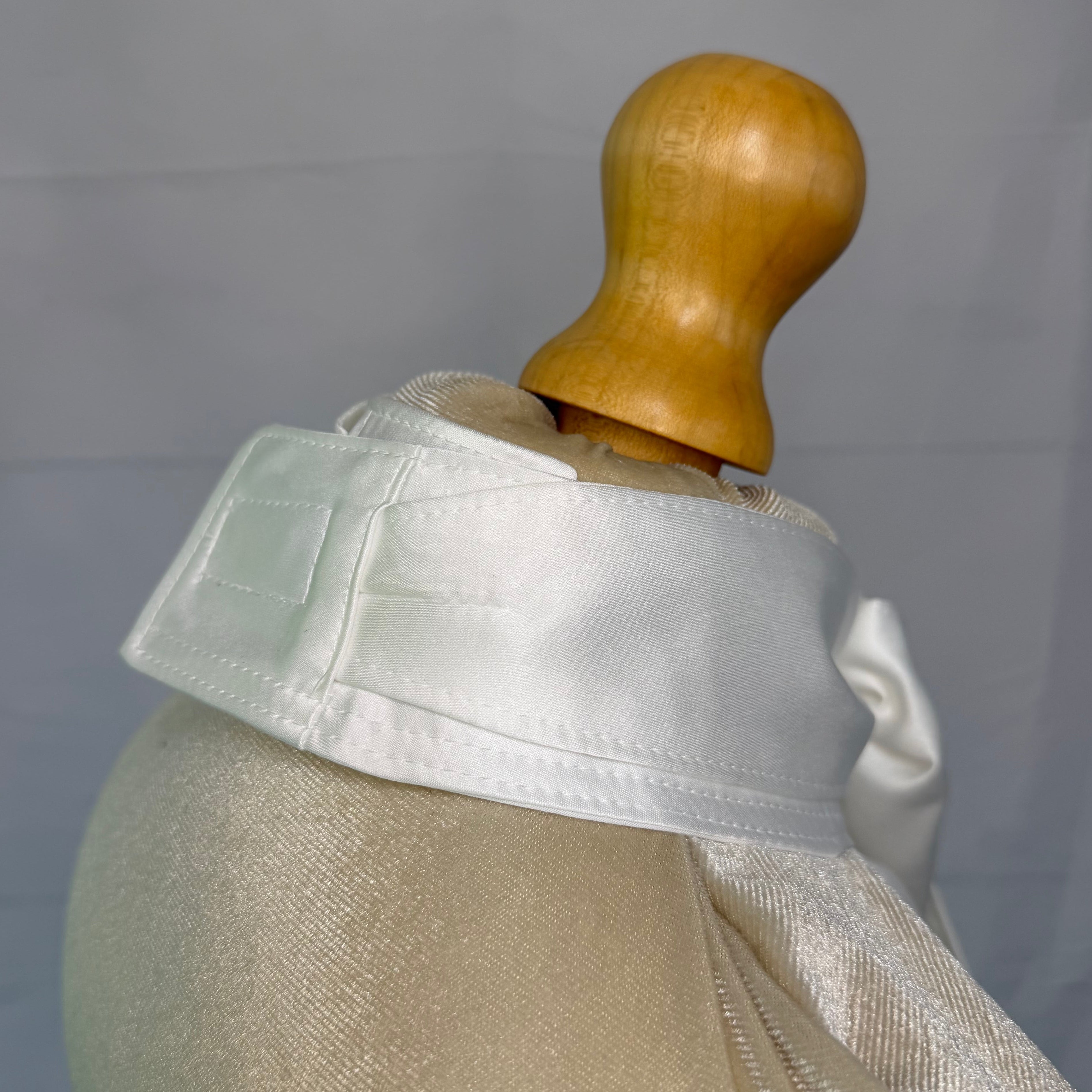 Mannequin wearing a light-colored stock tie with a wooden head on a plain background