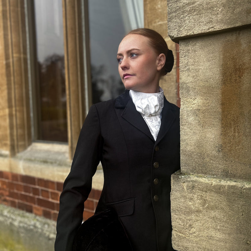 women in a black jacket wearing an equestrian ready tied stock tie outside building 